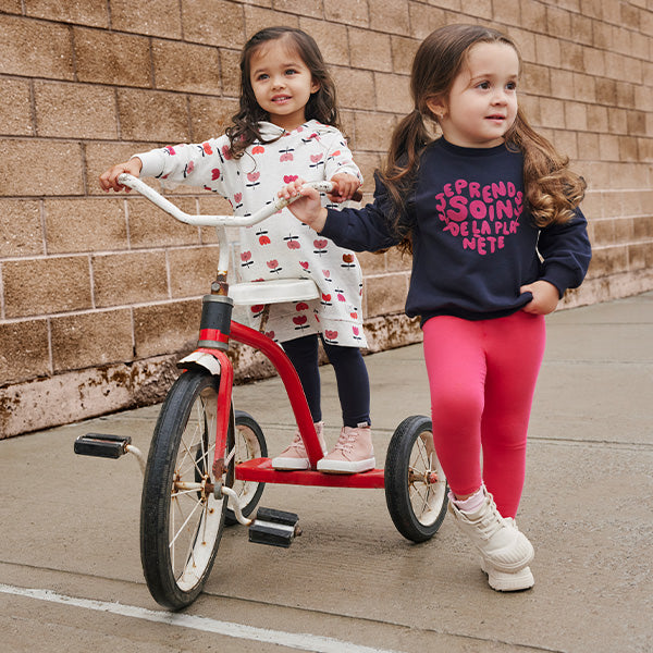 Enfants faisant du tricycle habillés avec des pantalons, robes, chandails et ensembles pour bébé.